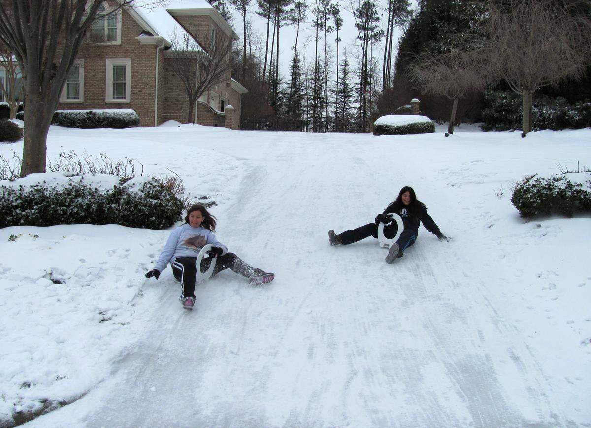 Monica Taggart and Jill Vandine use toilet seats to slide down a snowy driveway in Raleigh. The couldn’t find sleds for sale anywhere, so they got some toilet seats from Walmart. They work great.