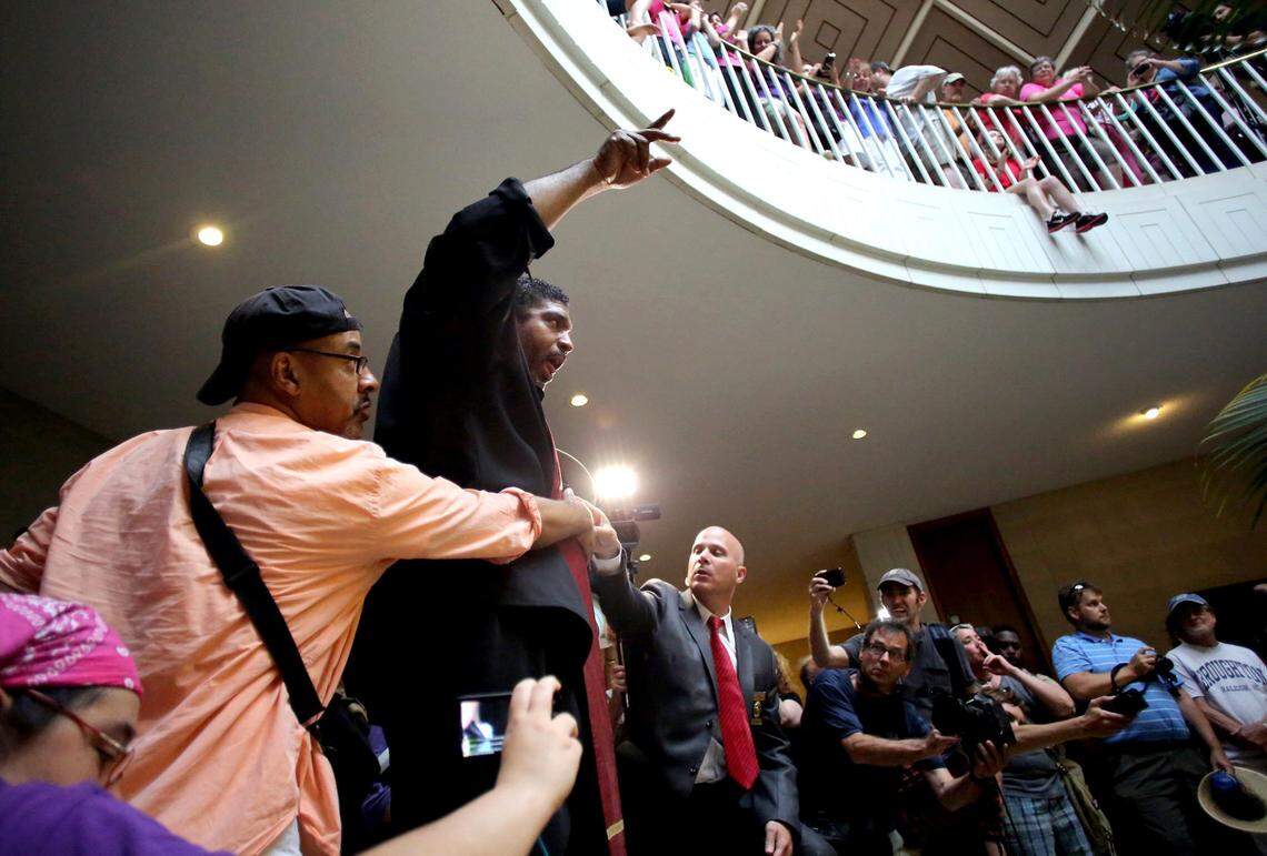 Rev. William Barber stands up on the ledge around the pool to tell observers not to boo the local authorities efforts to keep the crowd safe during the Moral Monday protests at the North Carolina Legislative Building in downtown Raleigh on Monday, July 8, 2013.