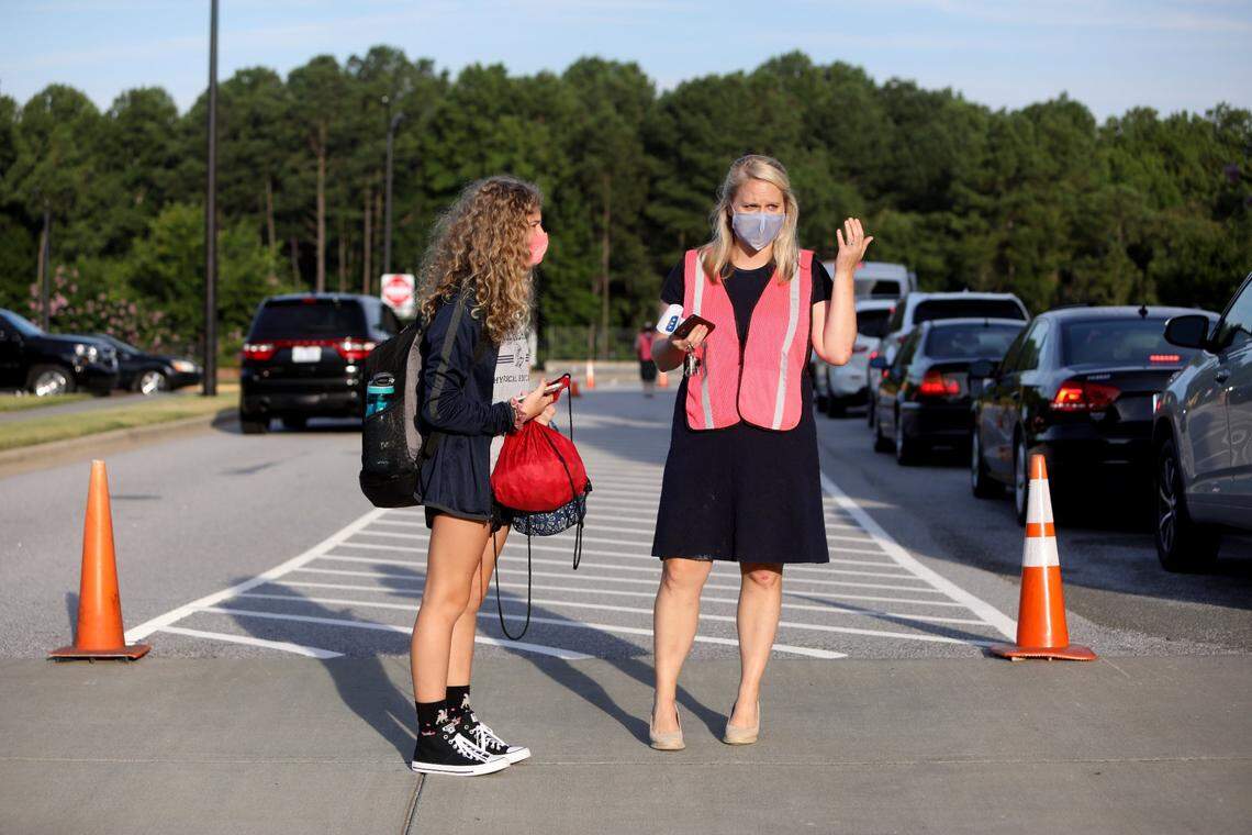 A Thales Academy student waits with school administrator Ashley Bahor, right, at the crosswalk after her temperature was checked in carpool on July 22, 2020, in Rolesville.