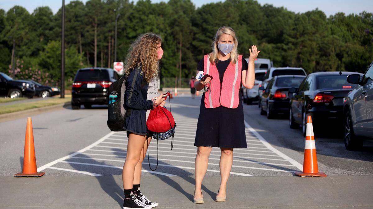 A Thales Academy student waits with school administrator Ashley Bahor, right, at the crosswalk after her temperature was checked in carpool on July 22, 2020, in Rolesville.