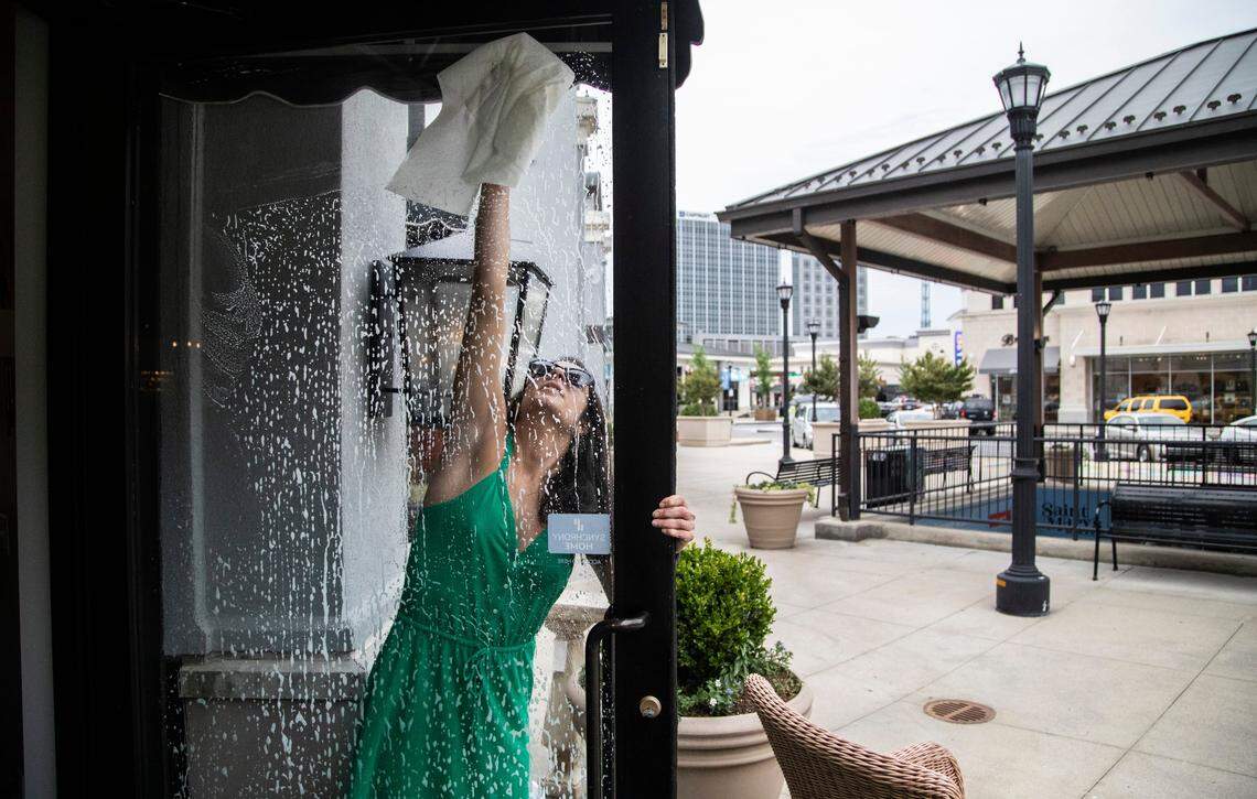 Danielle Partusch, manager and designer of Paysage, a boutique in North Hills in Raleigh, cleans the glass doorways as the store prepares to open their doors to the public Friday, May 8, 2020. Under the Phase 1 rules, non-essential businesses can open to customers at 5 p.m. Friday, May 8, at 50 percent capacity and with social distancing and strict cleaning rules in place.