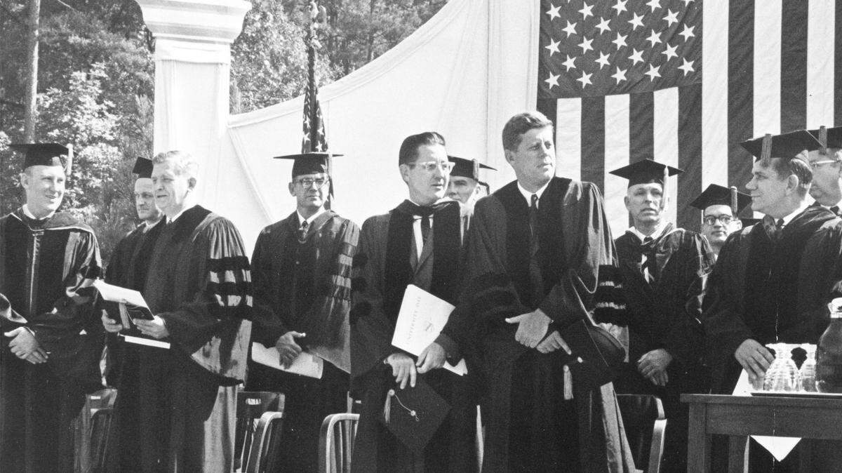 President John F. Kennedy waits on stage to receive an honorary doctor of laws degree from UNC on October 12, 1961.. On stage with him is Terry Sanford (second from left), William Friday (standing to Kennedy’s right), and William Aycock, right.