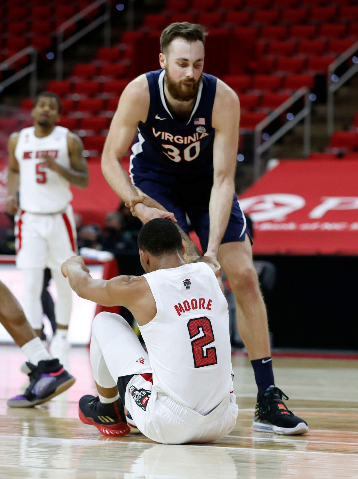 Virginia’s Jay Huff (30) helps up N.C. State’s Shakeel Moore (2) during the second half of Virginia’s 64-57 victory over N.C. State at PNC Arena in Raleigh, N.C., Wednesday, February 3, 2021.