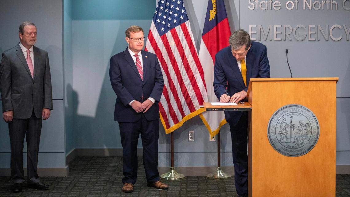 Gov. Roy Cooper signs coronavirus relief bills Monday in Raleigh as N.C. Senate Leader Phil Berger, left, and House Speaker Tim Moore look on during a briefing on the state’s coronavirus response.