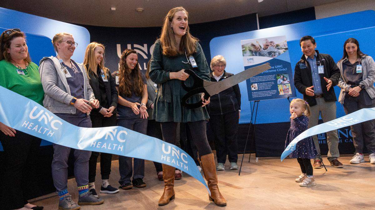 Pediatrician Kate Westmoreland cuts a ribbon during a ceremony Monday, March 17, 2025, for the opening of UNC Health’s new Down Syndrome Clinic in Chapel Hill as her daughter, Izabel, 2, who has Down syndrome, looks on. The clinic serves children and adults with developmental disabilities.