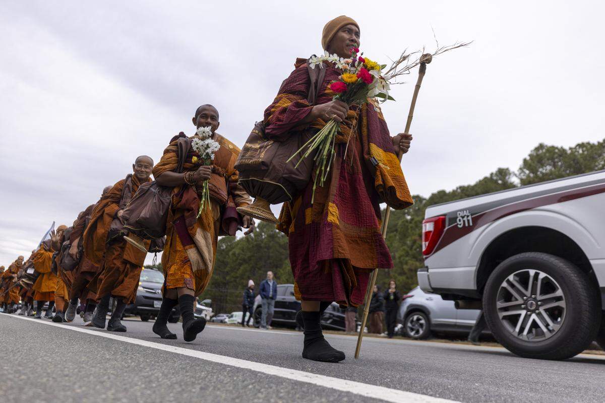 A procession of Buddhist monks walks along U.S. Highway 64 near Wilsonville on Friday, Jan. 23, 2026, as thousands of onlookers line the highway to welcome them. The monks are making a 2,300-mile pilgrimage from Texas to Washington, D.C., as part of the Walk for Peace, an effort to promote peace, compassion and national unity.