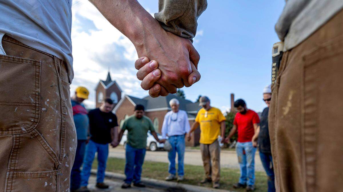 Members of IChurch from Hickory, N.C. pray with Bob Smith, center, a Trustee of the Old Fort United Methodist Church on Saturday, October 5, 2024 in Old Fort, N.C. More than four feet of water from Mill Creek flooded the building during Hurricane Helene. IChurch members volunteered their time on Saturday to shovel mud, and salvage items from the building.