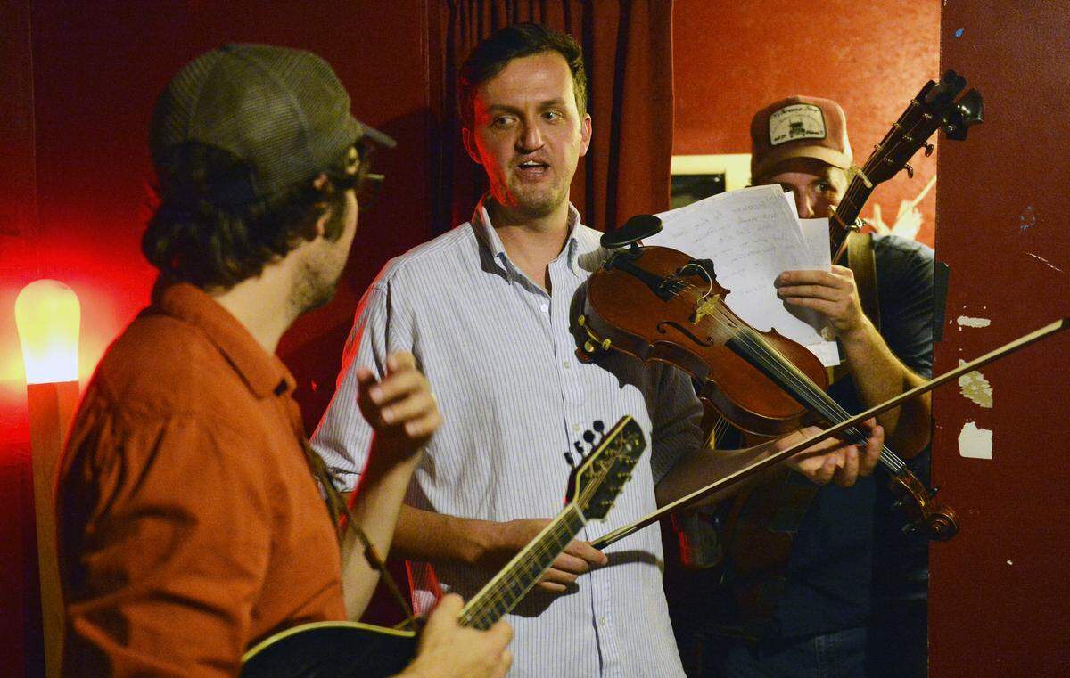 Bobby Britt (middle) of the band Town Mountain talks with close friend Andrew Marlin of the band Mandolin Orange (left) backstage at Cat’s Cradle as Town Mountain lead singer Robert Greer squeezes through with set lists before a show in August.