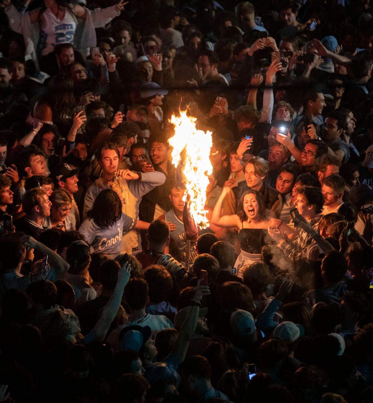 Celebrating Tar Heel fans cheer around a burning object in the intersection of Franklin and Columbia Streets in Chapel Hill, N.C. after UNC’s historic win against Duke in the Final Four on Saturday, April 2, 2022.