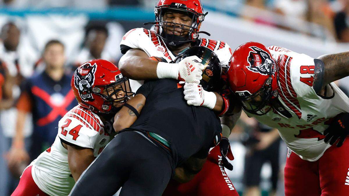 N.C. State defensive end Savion Jackson (90) wraps up Miami running back Jaylan Knighton (4) as Derrek Pitts Jr. (24) and Cory Durden (48) come in to help with the tackle during the first half of N.C. State’s game against Miami at Hard Rock Stadium in Miami Gardens, Fla. Saturday, Oct. 23, 2021.