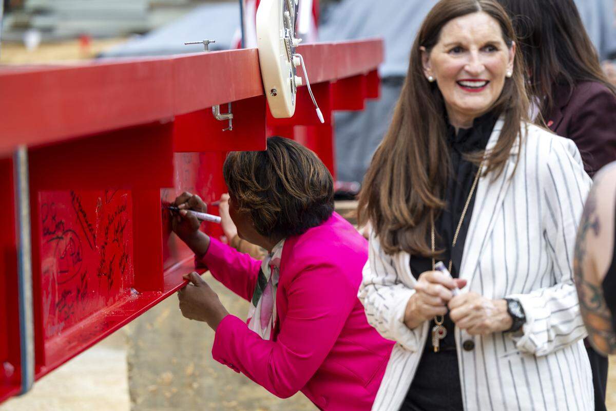 Raleigh City Manager Marchell Adams-David, left, and Kerry Painter, executive director of the Raleigh Convention and Performing Arts Complex, sign a steel beam before it is hoisted into place during a topping-out ceremony at the new Red Hat Amphitheater in downtown Raleigh on Tuesday, May 26, 2026. The new amphitheater is expected to open in spring 2027.