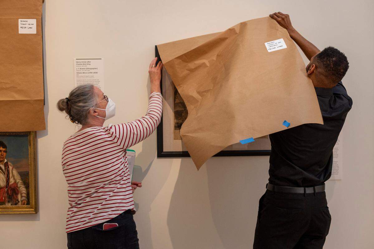 Maggie Gregory, Director of Collections Management and Chief Registrar, and Moses T. Alexander Greene, Director of preforming arts and film, cover an engraving, "Chief of the Cherokee” by Isaac Basire dating to 1730, to protect it from light on Sept. 20, 2022, in Raleigh.