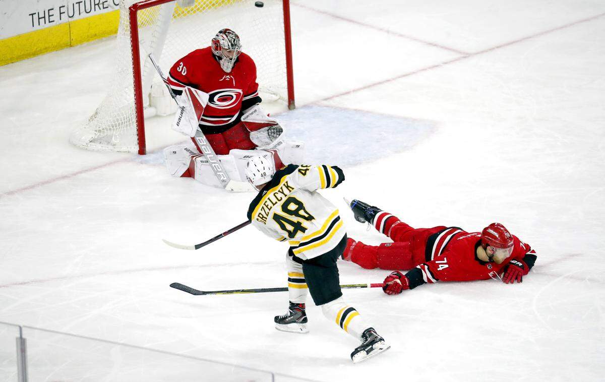 The Bruins Matt Grzelcyk (48) shoots the puck past the Canes' Cam Ward (30) and Jaccob Slavin (74) for a goal during the third period.  The Bruins beat the Canes 6-4.