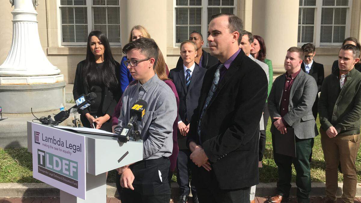 Connor Thonen-Fleck, a transgender 16-year-old who is one of the North Carolinians suing the State Health Plan, speaks at a press conference in Durham after the lawsuit was filed March 11, 2019. He is flanked by his dad Jason Fleck, right, and other lawsuit plaintiffs and supporters from pro-LGBT groups like Lambda Legal and Equality NC.