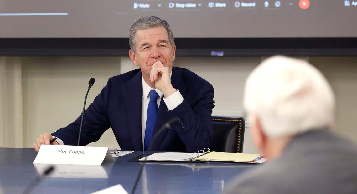 N.C. Gov. Roy Cooper smiles as he listens to Agriculture Commissioner Steve Troxler tell a story during the Council of State meeting in Raleigh, N.C., Tuesday, Jan. 9, 2024.