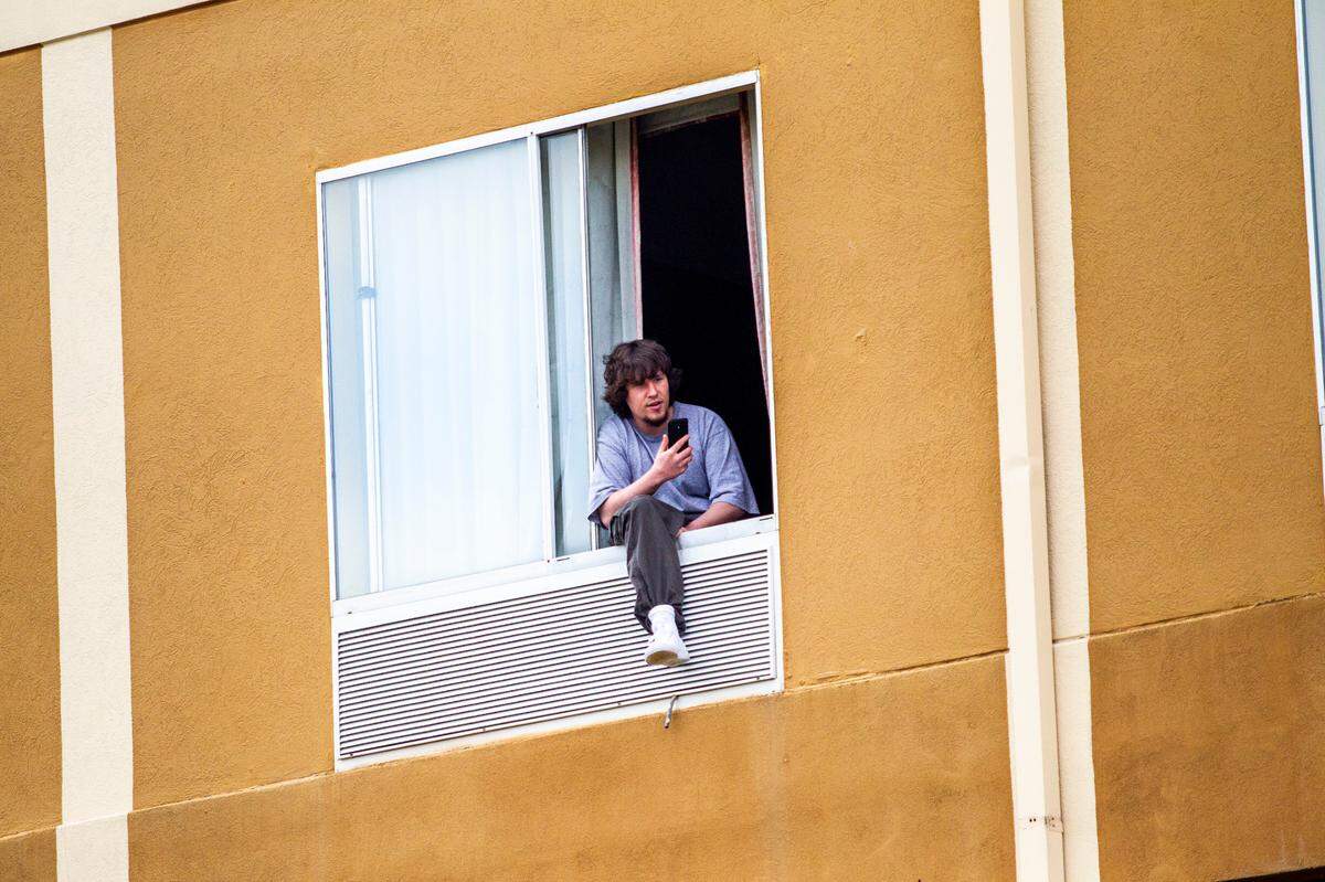 A man watches from inside a Quality Inn in Durham as about a dozen demonstrators protested outside the hotel Wednesday, March 24, 2021. Demonstrators were protesting living conditions and other concerns related to people being kept at the hotel after they are released from prison. State officials said the hotel was leased for men who are being released from a prison in which they could have been exposed to COVID-19 and who donÕt have another suitable housing plan.