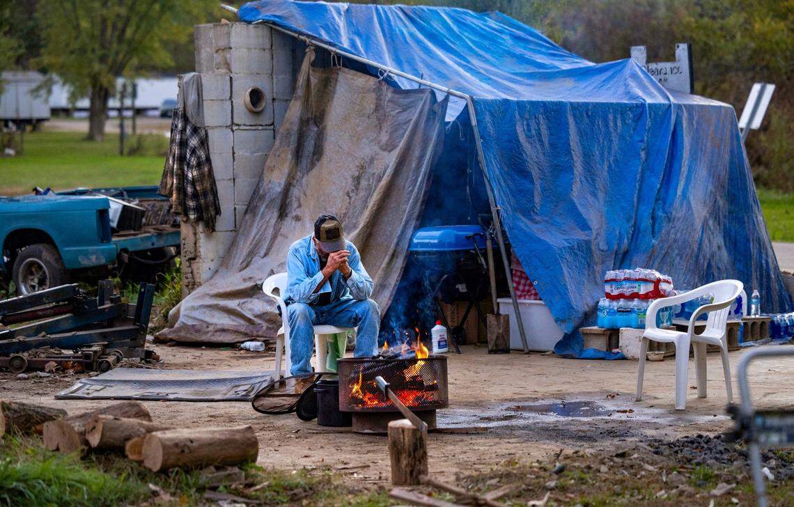 Quint Earl Barker warms himself by a fire at his property on Broad Street on Oct. 16, 2024 in Clyde. Barker lived in the back of the historic family home that dates to the late 1800s. After the storm, Barker said he was overwhelmed with the outpouring of support from the community. He pitched a second tent to house his abundance of supplies.