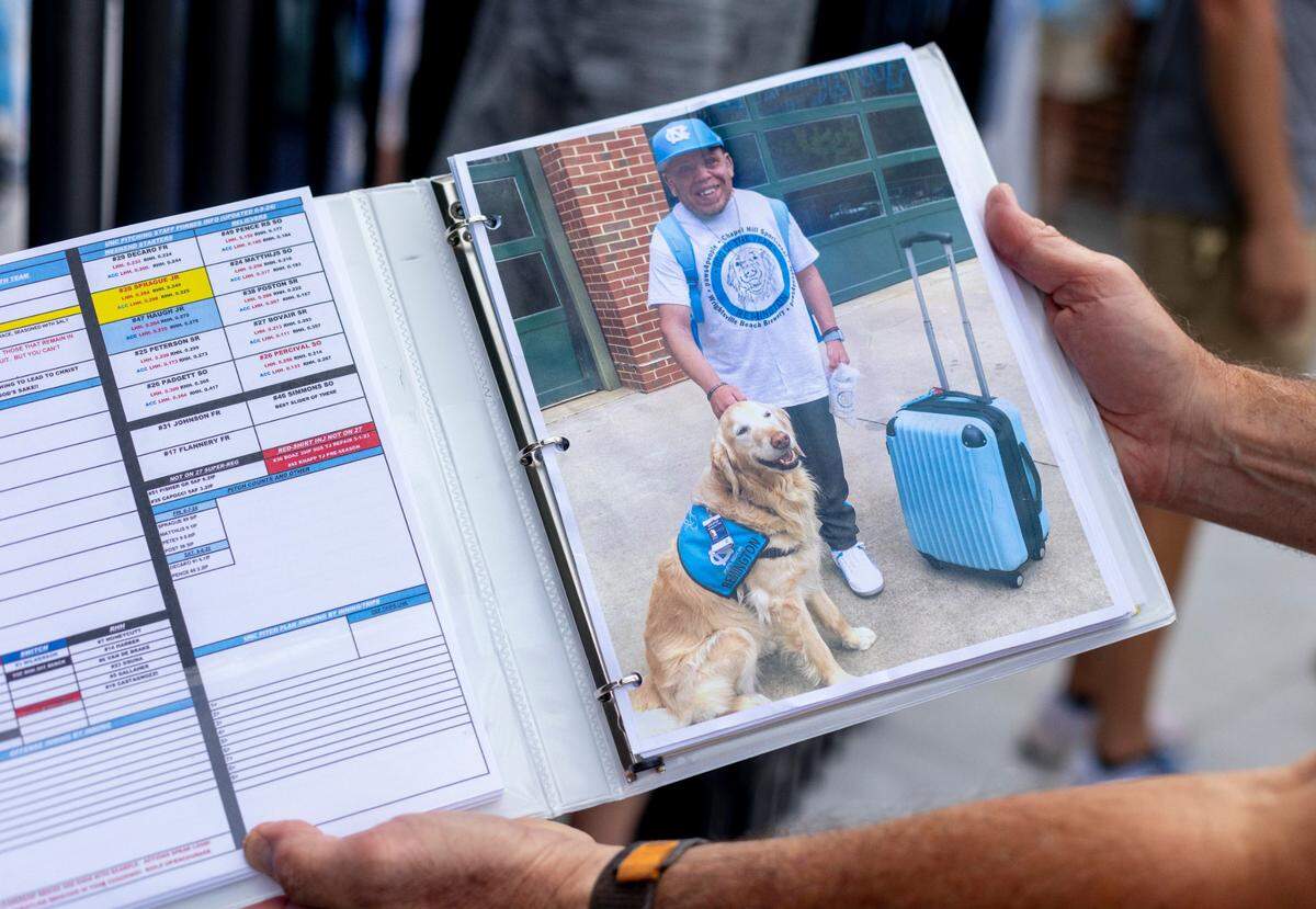 North Carolina baseball coach Scott Forbes displays a photo of J.R. Anton in one of his game notebooks he has packed for the trip to the College World Series on June 11, 2024 at Boshamer Stadium in Chapel Hill. J.R. Anton became a friend of the Tar Heel baseball program in 2006 during the CWS in Omaha. After his death, the players wrote J.R.’s initials on their game caps as a tribute to him.