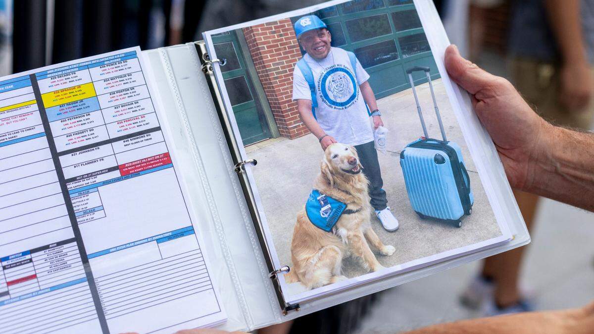 North Carolina coach Scott Forbes displays a photo of J.R. Anton in one of his game notebooks he has packed for the trip to the College Word Series on Tuesday, June 11, 2024 at Boshamer Stadium in Chapel Hill, N.C. J.R. Anton became a friend of the Tar Heel baseball program in 2006 during the College World Series in Omaha. Upon his death last month, the players have all written J.R.’s initials on their game caps as a tribute to him.