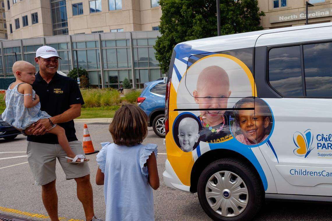 Gracie, in the middle, looks at CCP’s new van which is printed with her face in one of the children portrait. On the left is Perry Coxe who hold Perry in the arms. Perry is one of the children portrait printed on the side of the van.