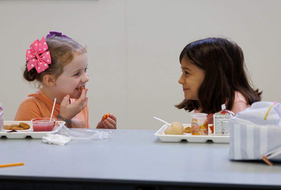 Burton Elementary School second-grade students Audrey White and Eliza Oltmans share a smile during lunch on Thursday, Sept. 5, 2024, in Durham, N.C. This year, Durham Public Schools became the largest school district in the state to offer free meals to all students.