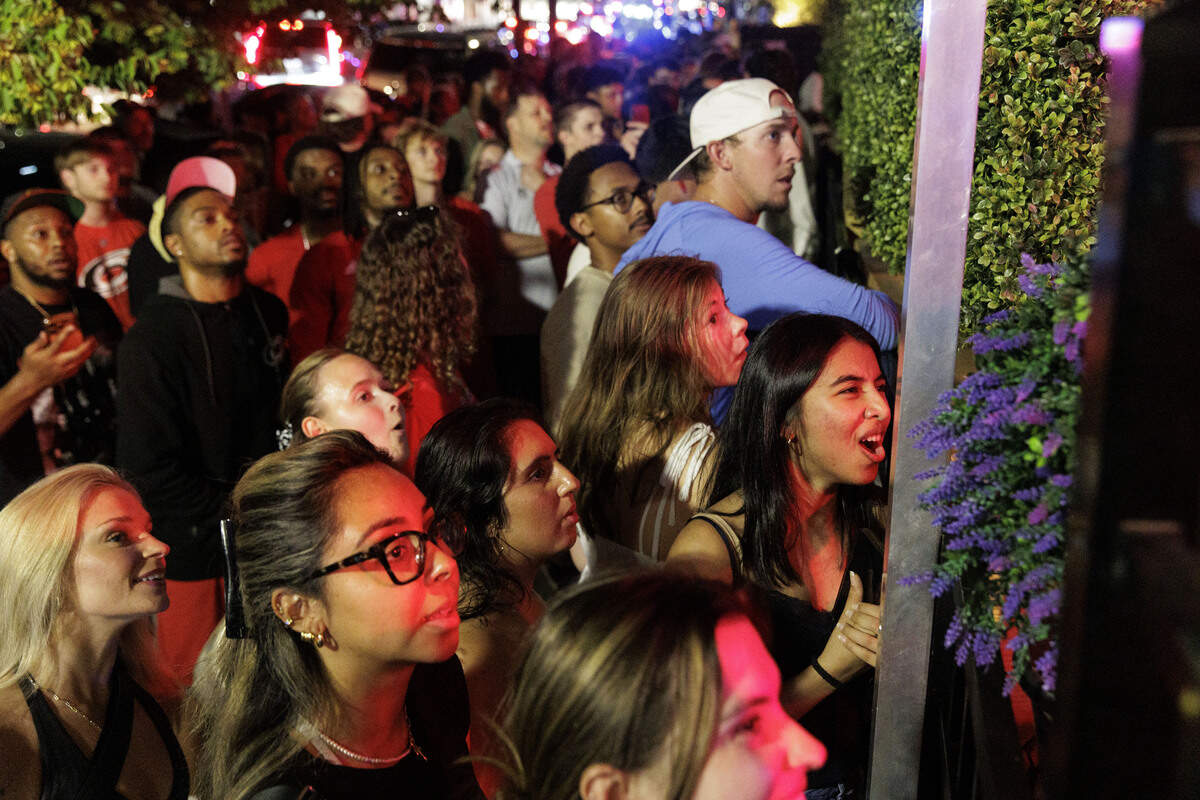 Fans peeked through gaps in the fence to watch Stanley Cup finals post-game on the TV at Teets bar after the Carolina Hurricanes won their second Stanley Cup in Glenwood South District on June 14, 2026, in Raleigh, North Carolina. The Hurricanes last won in 2006.
