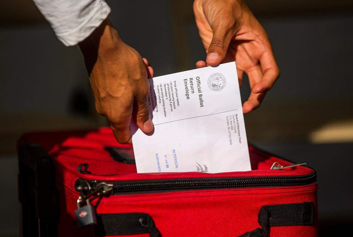 Volunteer Hayden Baker drops an absentee ballot into a locked box under a tent set up outside the Durham County Board of Elections, on Thursday, Oct. 8, 2020, in Durham, N.C.