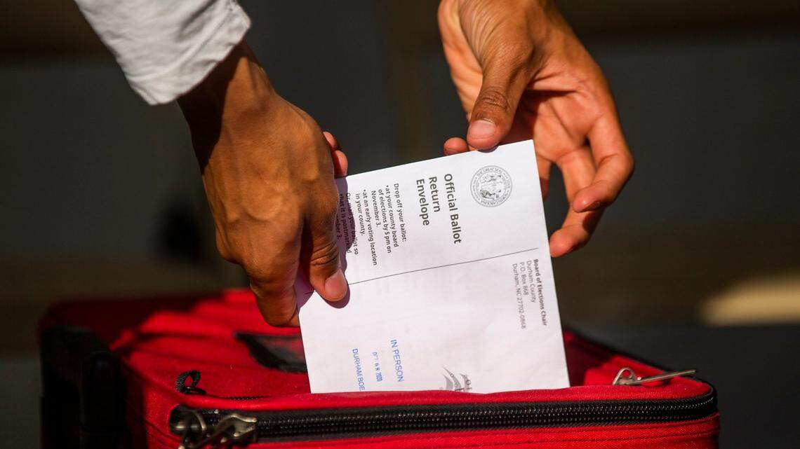 Volunteer Hayden Baker drops an absentee ballot into a locked box under a tent set up outside the Durham County Board of Elections, on Thursday, Oct. 8, 2020, in Durham, N.C.