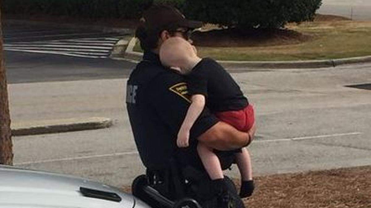 A Fayetteville police officer holds a child found in a car in 2021 with his unconscious parents, who had had overdosed on heroin. (Fayetteville Police Dept.)