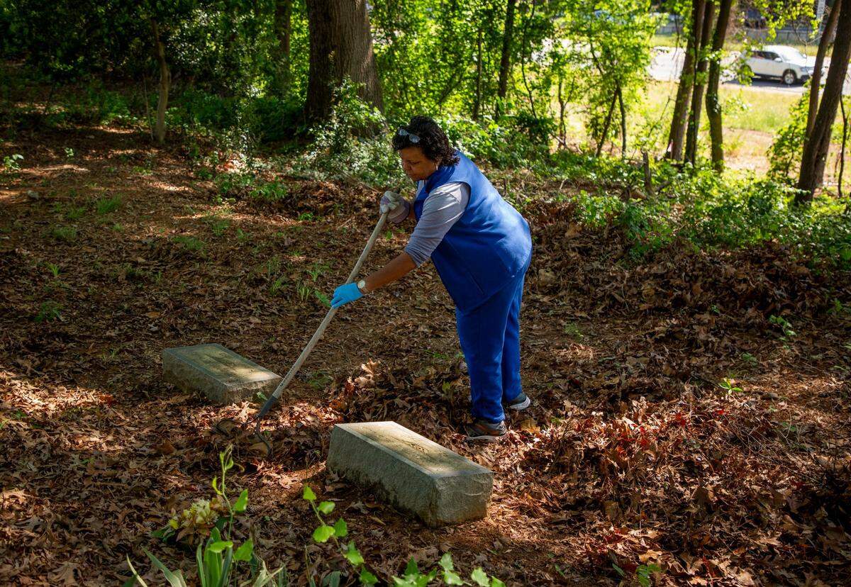 Deborah Lofton rakes leaves away from graves of her family members in the Oak Grove Cemetery, which was founded by freed African-Americans after the Civil War and now has lost more of its tree buffer to widening of the I-440 Beltline, that separated it from the rest of the Method community in the 1960s, on Saturday, May 8, 2021, in Raleigh, N.C.
