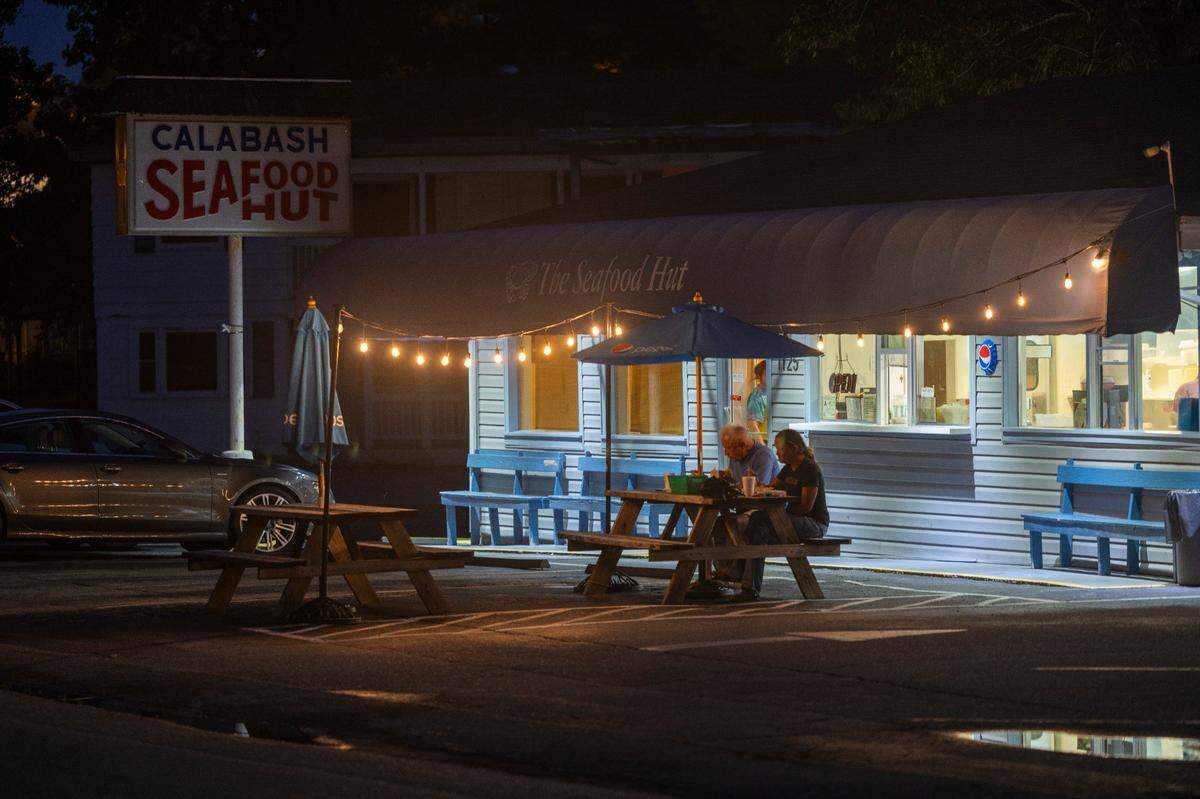 Just after 9 p.m. the last customers at the Seafood Hut dine beneath the lights at one of the many outdoor tables on Thursday, June 27, 2024 in Calabash, N.C.