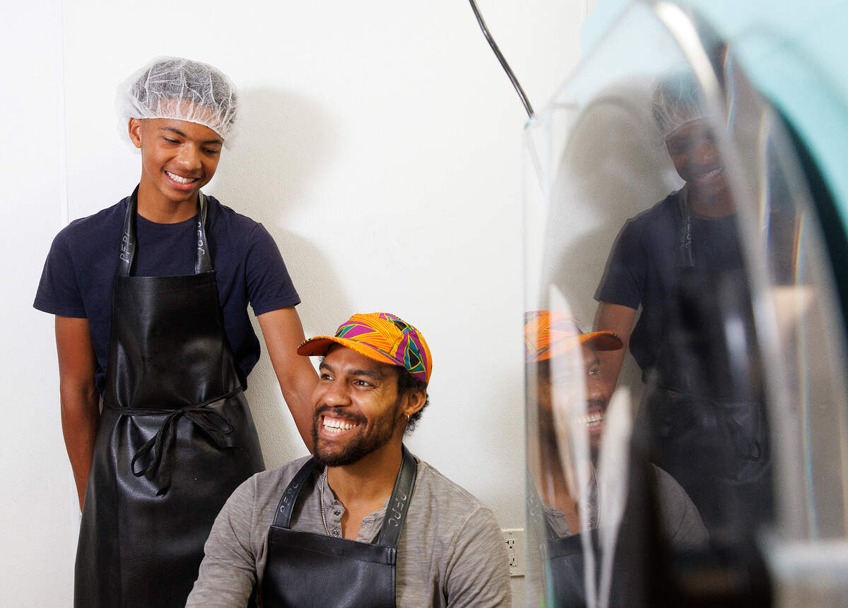 Pierce Freelon, right, and his son, Justice, 15, are reflected in the window of a freeze dryer at Piedmont Food Processing Center in Hillsborough, N.C. on Tuesday, June 4, 2024. Freelon produces Coco Fro, vegan freeze-dried ice cream.