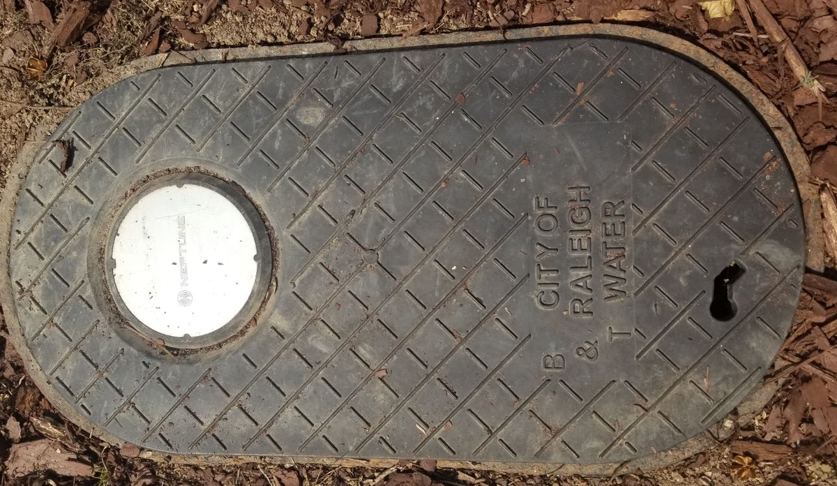The silver disc on city of Raleigh water meter boxes functions as an antenna for handheld receivers to record water usage.
