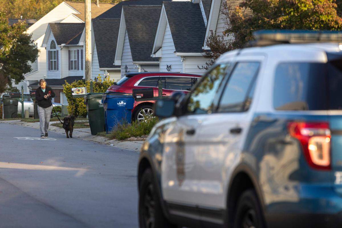 A resident of Castle Pines Drive in the Hedingham neighborhood walks their dog on Friday morning, October 14, 2022 in Raleigh, N.C. as law enforcement continue to investigate the killing of five people yesterday on the greenway nearby.