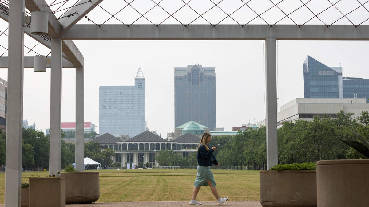 State employee Corrie Byrd walks around the Halifax Mall, behind the North Carolina General Assembly building, with a hazy downtown skyline backdrop, as smoke from Canadian wildfires moves across the country on Wednesday, June 7, 2023 in Raleigh, N.C. The smoke is expected to mostly clear the area on Friday.