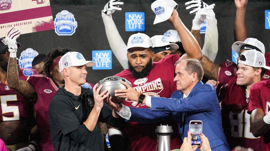 Florida State Seminoles head coach Mike Norvell is handed the ACC Championship trophy by ACC Commissioner Jim Phillips after defeating Louisville at Bank of America Stadium in December 2023.