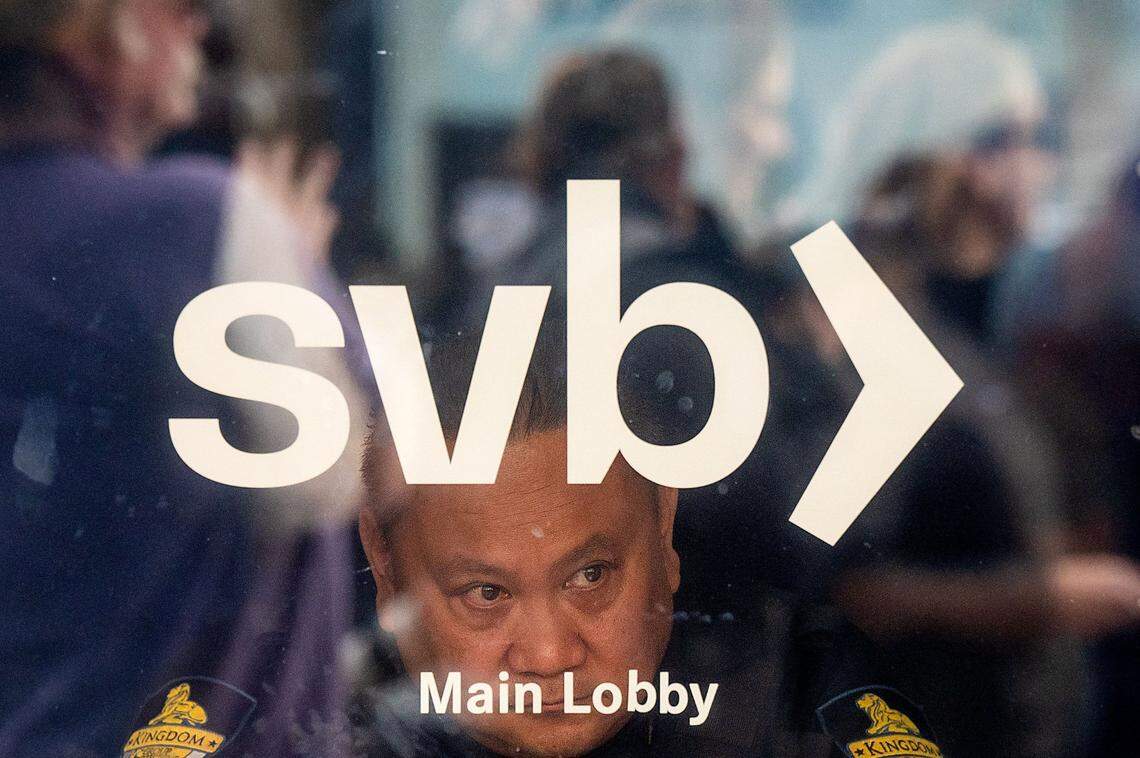 A security guard looks out a door as customers line up at Silicon Valley Bank headquarters in Santa Clara, California, on March 13, 2023.