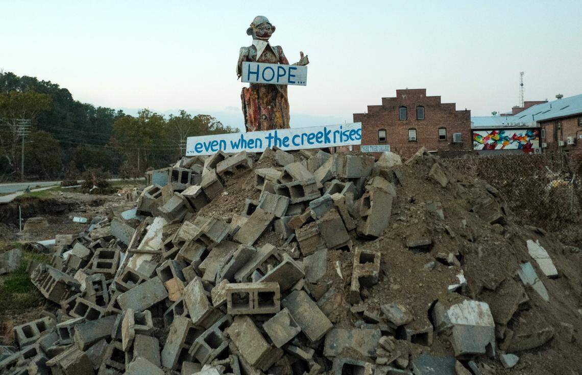 Asheville’s River Arts District suffered some of the most catastrophic damage during Hurricane Helene. A city official said recently that 80 percent of the district was destroyed. In the days after the storm a makeshift statue was erected off of Lyman Street, next to the French Broad River. The figure stood atop a pile of cinder blocks and held a sign that spoke not only for the city, but the entire region.