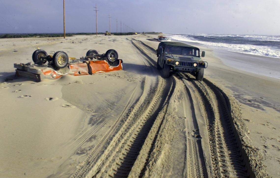 A North Carolina Army National Guard vehicle makes its way past an overturned truck partially buried in the sand on a section of what used to be Highway 12 just north of Buxton following Hurricane Dennis.  The National Guard was bringing much-needed supplies to Buxton and other communities cut off by sand and over wash.