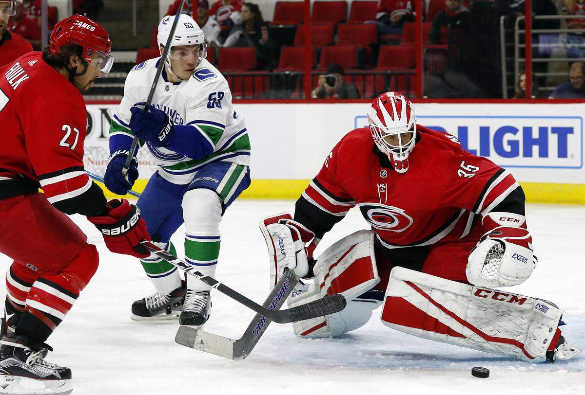 Carolina Hurricanes goaltender Curtis McElhinney (35) eyes the puck as teammate Justin Faulk (27) and Vancouver Canucks’ Bo Horvat (53) look on during the first period of an NHL hockey game, Tuesday, Oct. 9, 2018, in Raleigh, N.C.