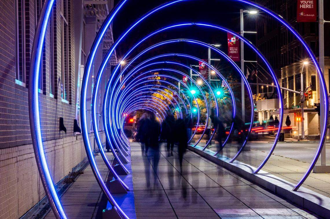 Pedistrians walk through the “Sonic Runway” along South Saunders Street in downtown Raleigh Friday, Dec. 2, 2022. The large-scale, interactive light-based art piece is one of 18 installations around downtown Raleigh and the Glenwood South district that make up the Illuminate Art Walk presented by Wake Tech.
