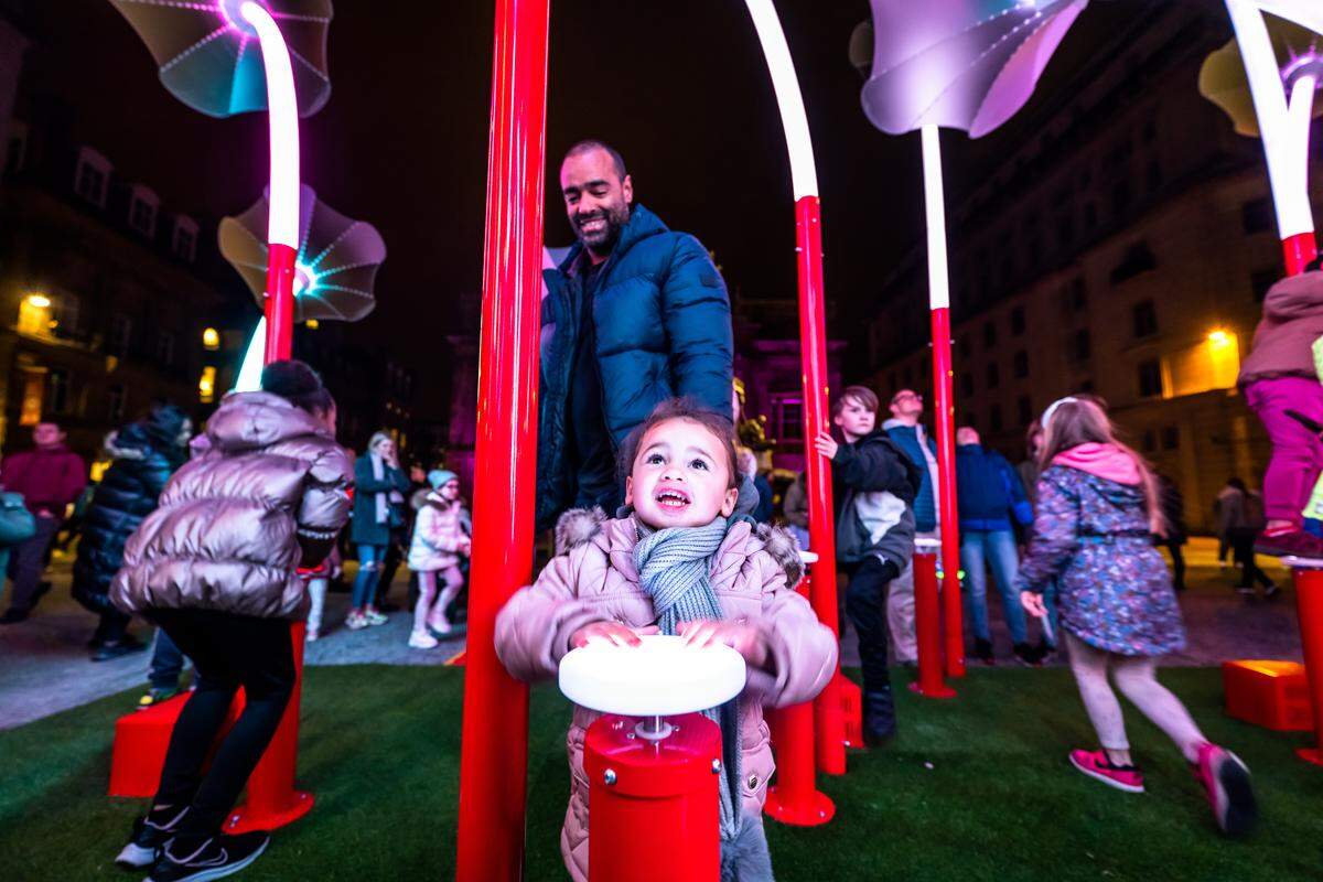 A child hits a button to make the ‘Trumpet Flowers’ play music. The piece is the featured artwork of the 2025 Illuminate Art Walk in downtown Raleigh.