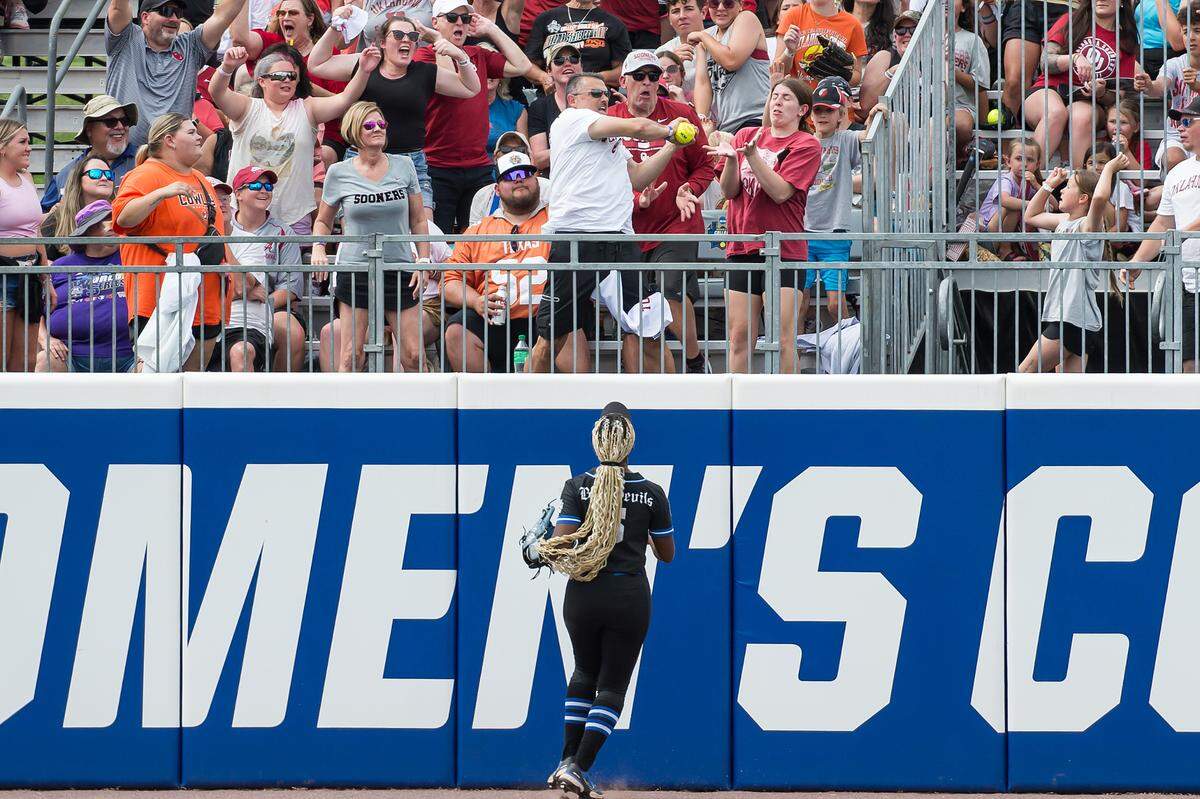May 30, 2024; Oklahoma City, OK, USA; Fans go after the home run ball of Oklahoma Sooners catcher Kinzie Hansen (not pictured) as Duke Blue Devils outfielder Amiah Burgess (5) looks on in the third inning during a Women’s College World Series softball game at Devon Park. Mandatory Credit: Brett Rojo-USA TODAY Sports