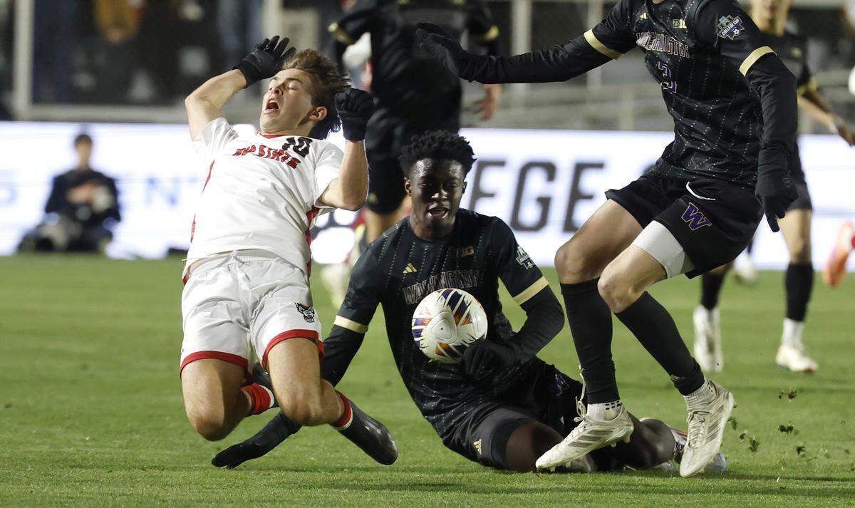 N.C. State's Taig Healy (10) goes down after being tackled by Washington's Osato Enabulele (21) during the first half of N.C. State’s game against Washington in the 2025 Men’s Soccer National Championship at WakeMed Soccer Park in Cary, N.C., Monday, Dec. 15, 2025.