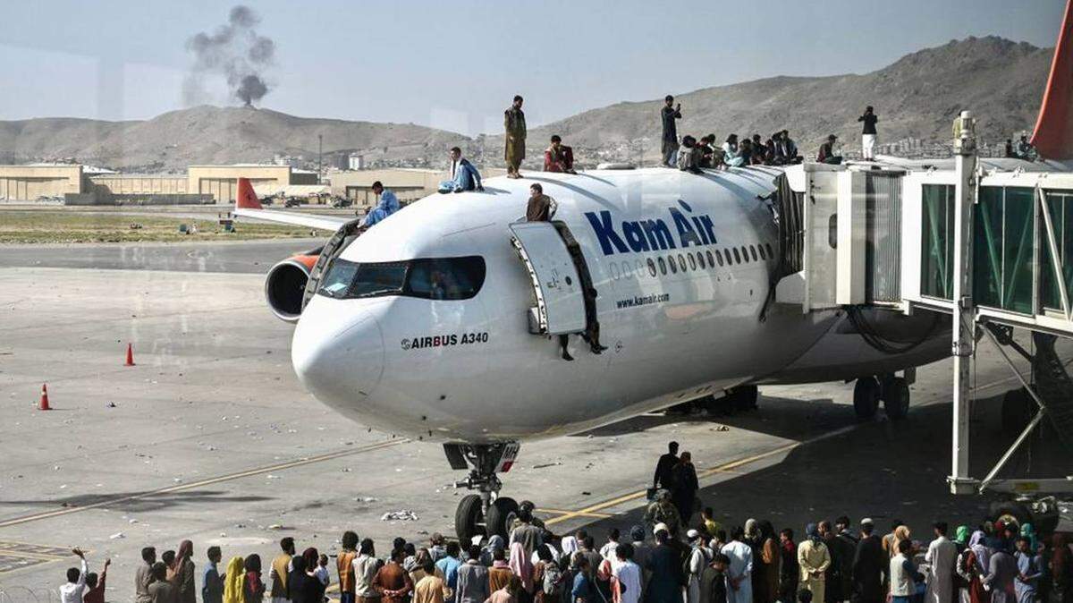 Afghan people climb atop a plane as they wait at the Kabul airport in Kabul on Aug. 16, 2021, after a stunningly swift end to Afghanistan’s 20-year war. Thousands of people mobbed the city’s airport trying to flee the Taliban’s feared hard-line brand of Islamist rule. 