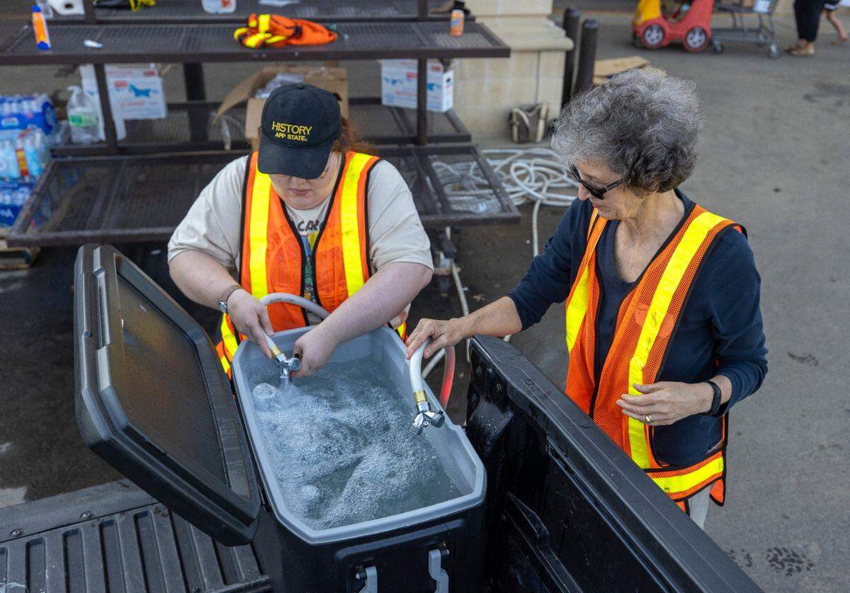 Volunteers Melissa McElwee and Tisa Lewis fill a cooler of water for a family without running water in the wake of Hurricane Helene, at the Ingles store on NC 9 on Tuesday, October 8, 2024 in Black Mountain, N.C.