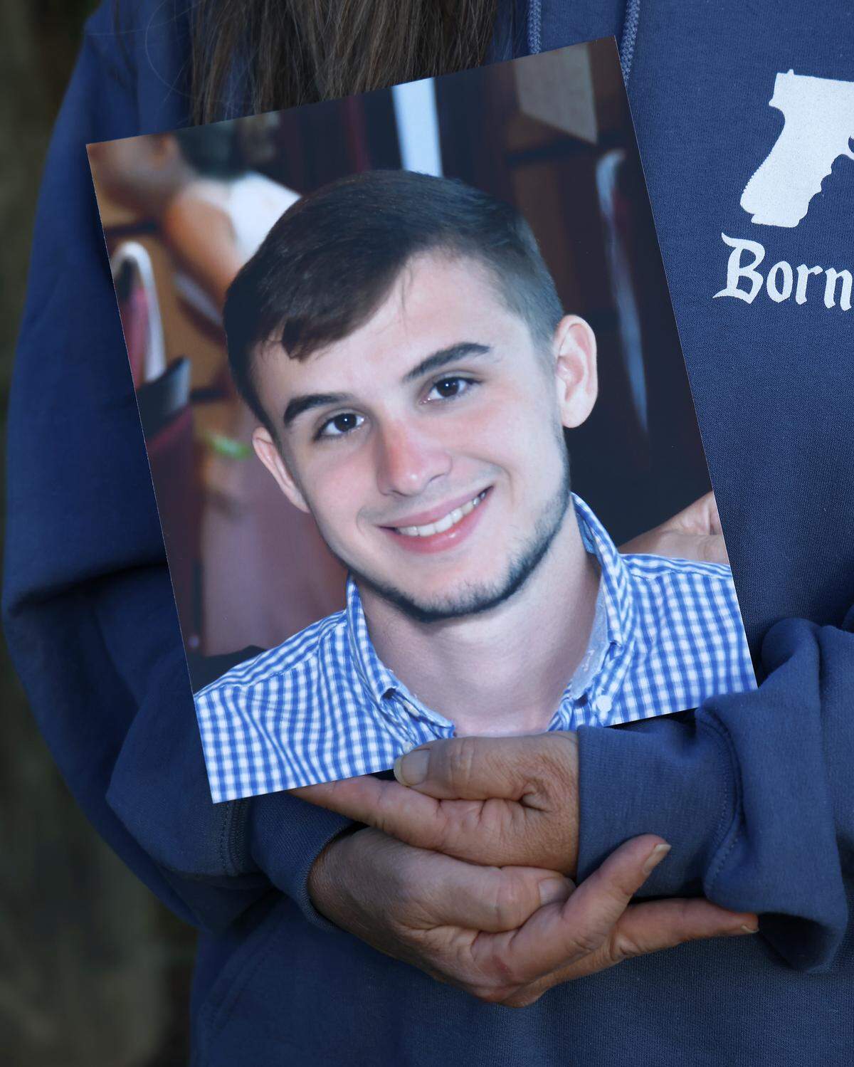 Lisa Higgins holds a photograph of her son, Michael Higgins, while standing next to his roadside memorial on Friday, Nov. 15, 2025. Michael, a Highway Patrol intern, died after a trooper reached 113 mph and lost control of his patrol car on a rural Pitt County road in August 2020.