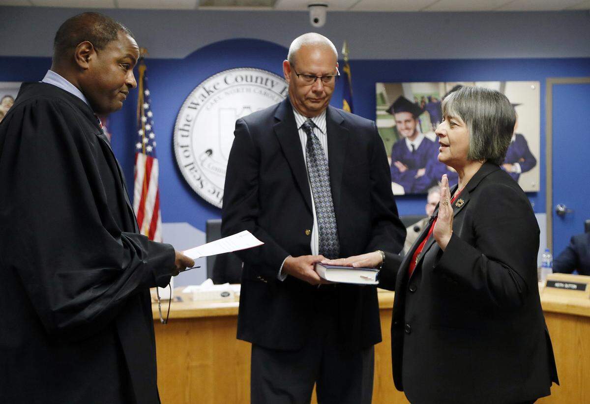 Judge Craig Croom, left, administers while husband Tommy Moore, center, assists as Catty Moore, right, takes the oath of office as the new Wake County superintendent at the school board’s May 23, 2018 meeting.