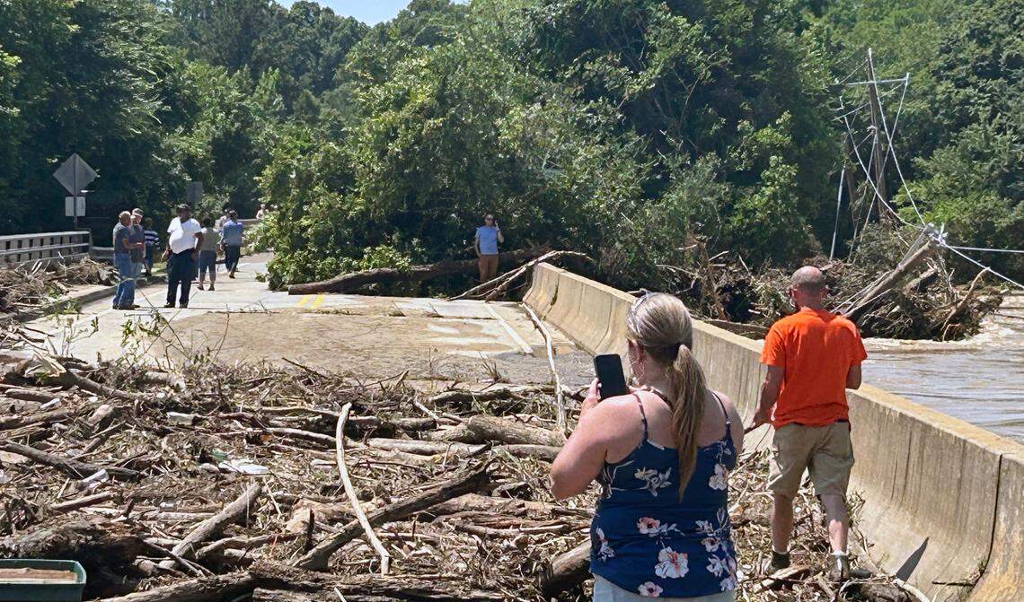 People make their way across the bridge over the Haw River through debris left by flood waters from Chantal. Damaged power lines are at right.