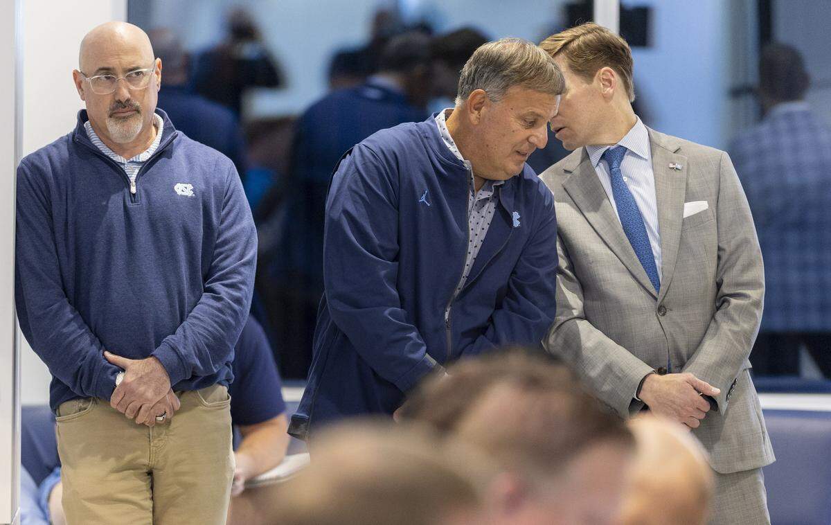 As Executive Associate Athletic Director Steve Newmark, left, listens to North Carolina coach Bill Belichick, North Carolina chancellor Lee Roberts talks with North Carolina football general manager Michael Lombardi during Belichick’s news conference on Monday, Oct. 13, 2025 at Kenan Stadium in Chapel Hill, North Carolina.